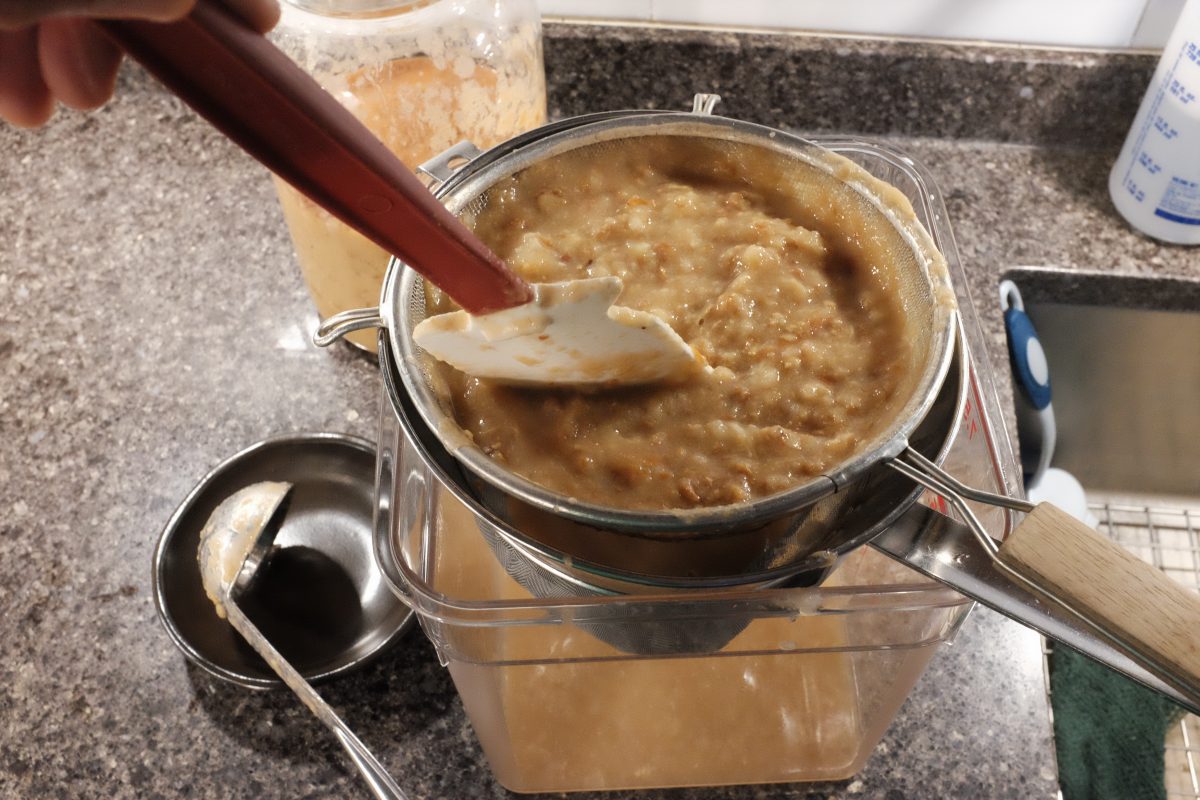 demonstrating stirring and pressing to get mash through strainers