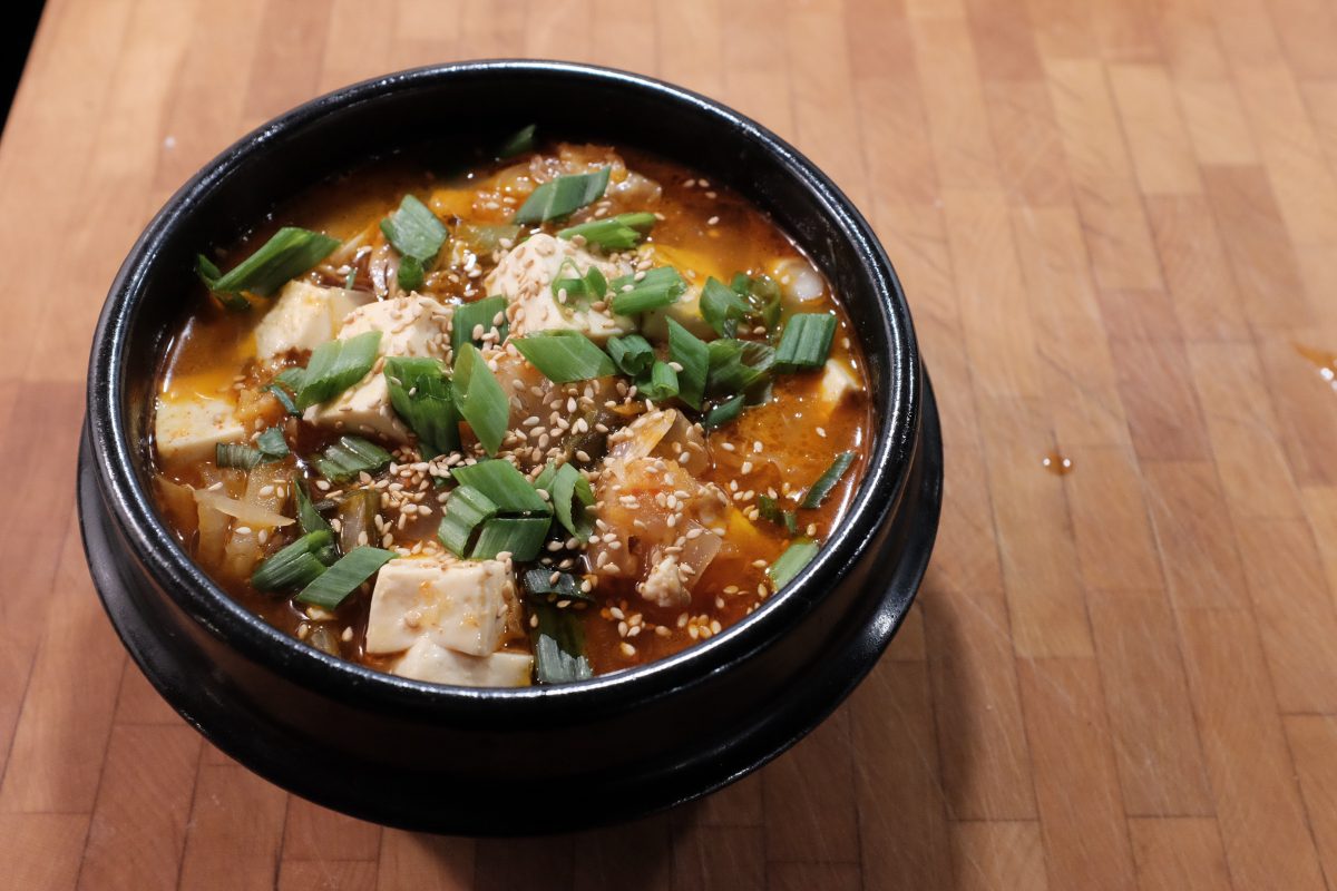the finished stew in a black bowl garnished with chopped green onion, sesame seeds and sesame oil